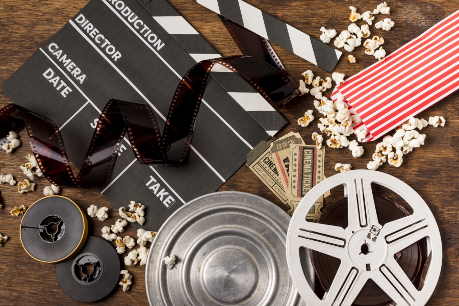 negatives-stripes-with-clapperboard-film-reels-tickets-and-popcorn-on-wooden-desk